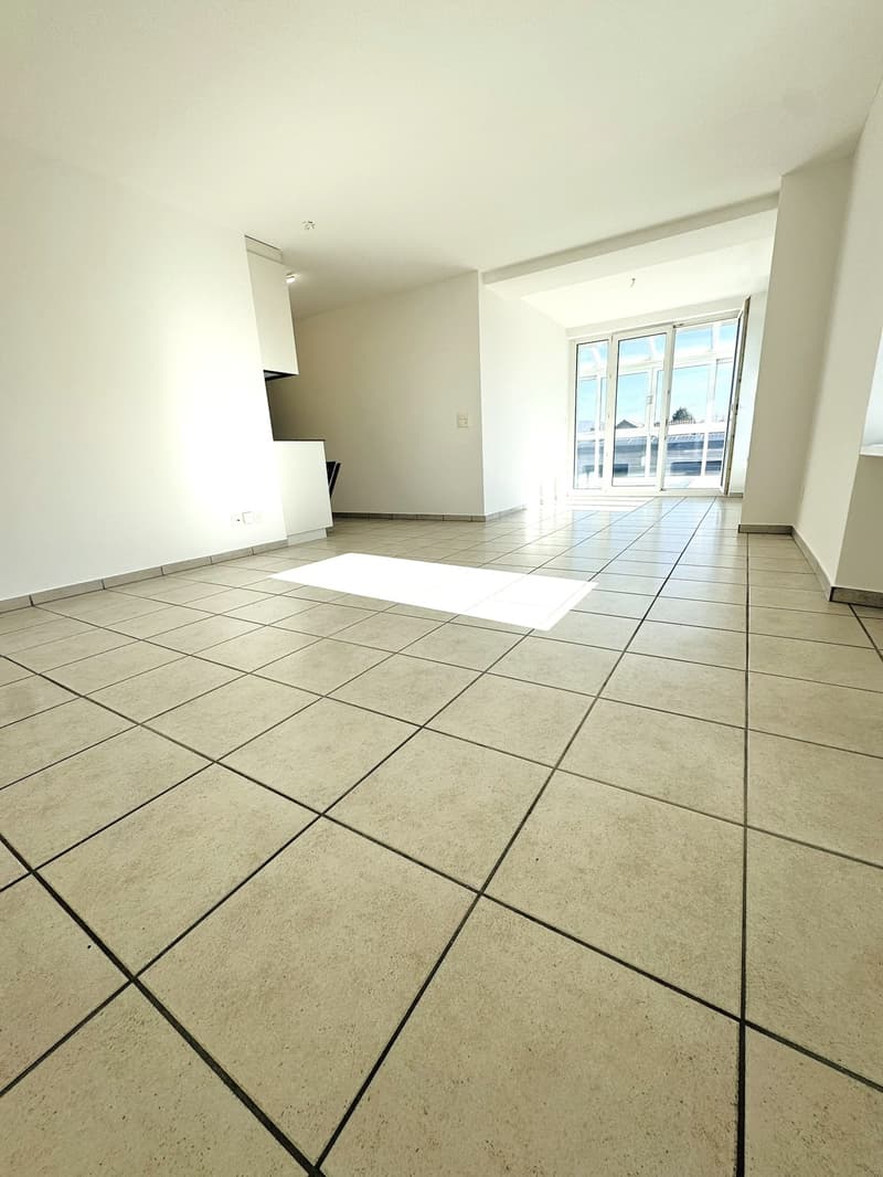 An empty room with white walls, tiled floor, and a glass door leading to a balcony. There are power outlets on the wall and a small white mat on the floor.