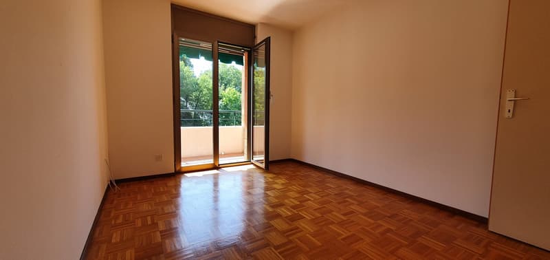 Empty room with hardwood floors, glass door leading to balcony, electrical outlet