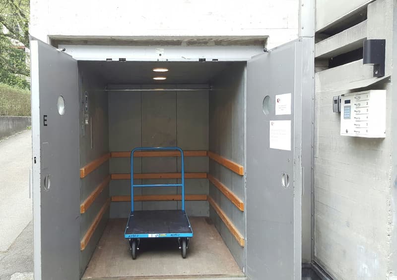 Concrete elevator shaft with wooden steps, blue hand truck, and control panels on the wall