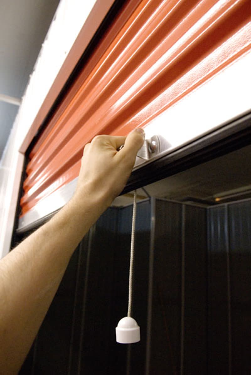 The image shows a hand pulling open an orange curtain or blind, revealing a dark room behind it.