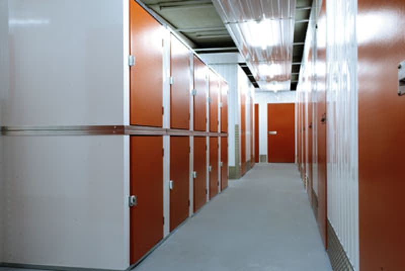 Long hallway with multiple storage units or lockers on both sides, with white walls and a concrete floor.