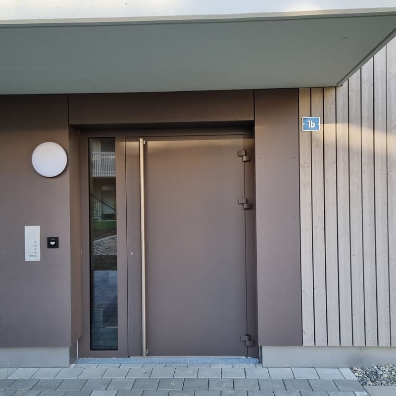 Raised ground floor, grey concrete, front door, brown wood paneling, large round light