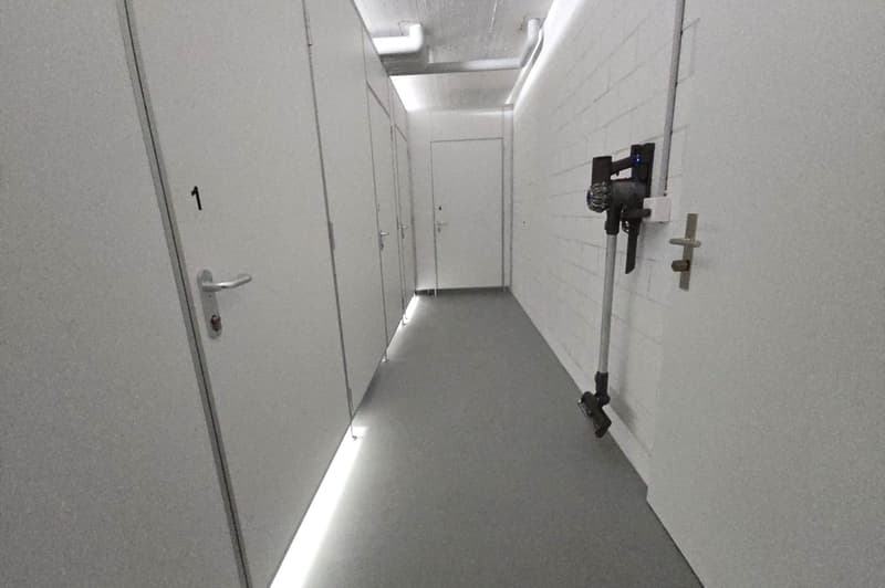 Corridor with storage units on both sides, white walls, gray floor, two doors, white ceiling, bright lighting.