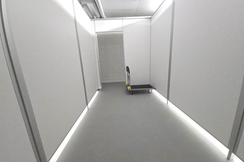 Empty storage unit room, white walls, grey floor, white lighting strip on sides