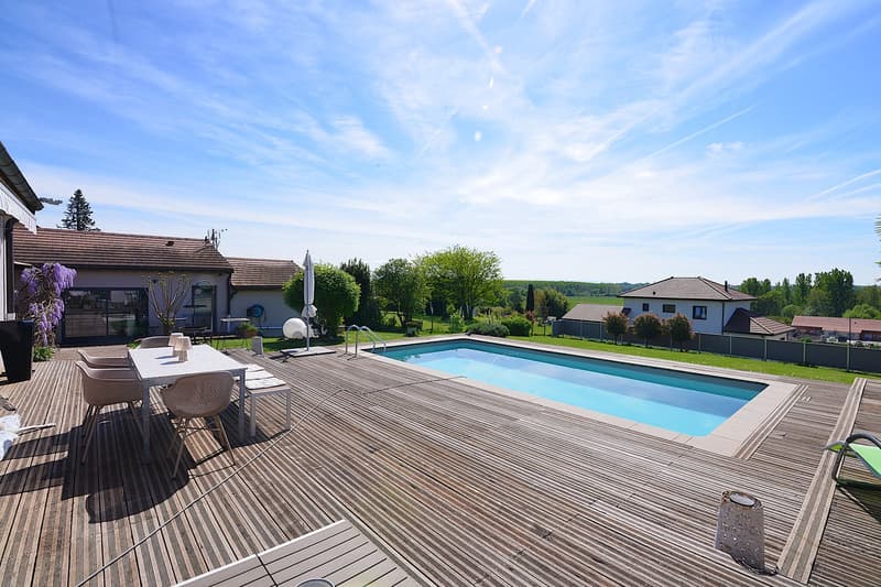 wooden deck, outdoor dining table, swimming pool, green lawn, distant houses, trees, clear sky