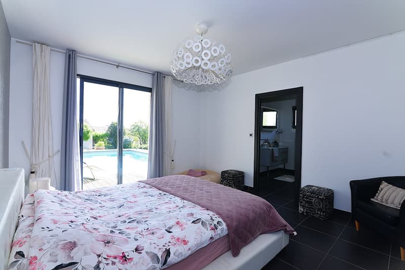 white walls, black floor, large bed, white ceiling lamp, sliding glass door, pool view