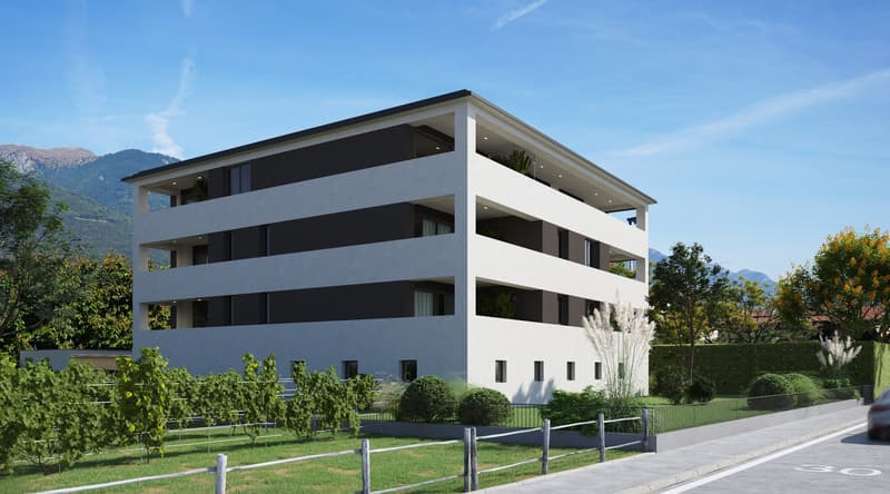 A modern, multi-story apartment building with a white exterior and black accents. The building has multiple floors and balconies, and is surrounded by landscaped gardens and a parking area.