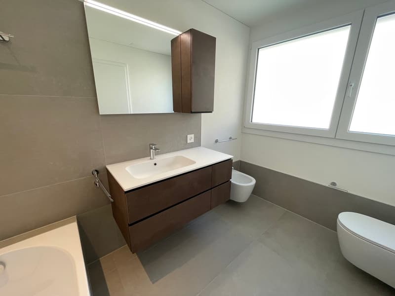 modern bathroom with large mirror, double sink, toilet, bathtub, and window