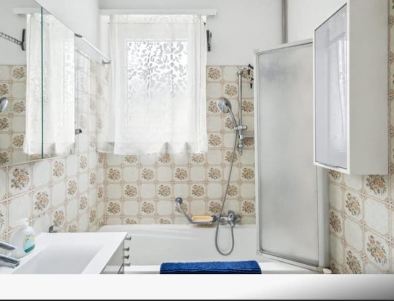 White bathroom with tiled walls, glass door shower, bathtub, sink, and towel