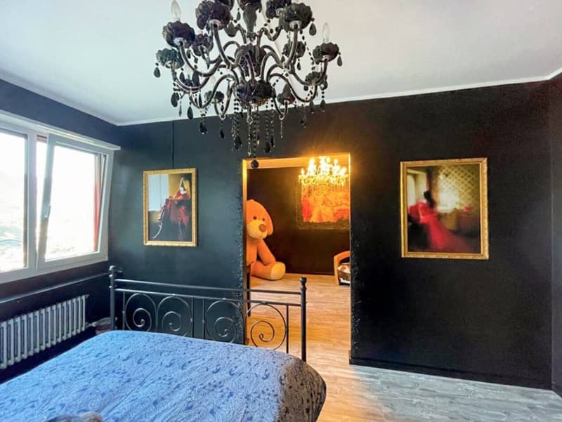 black walls, large double bed, large chandelier, teddy bear, radiator, window, framed picture, hallway