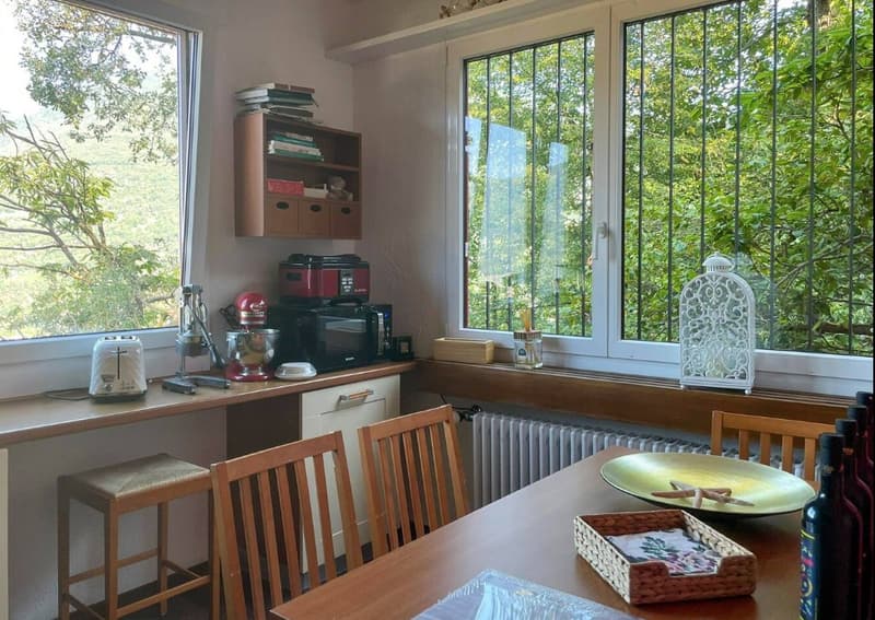 4 chairs around a dining table, 1 bookshelf, microwave, toaster, wooden desk with a mixer, a bottle, and wine bottles