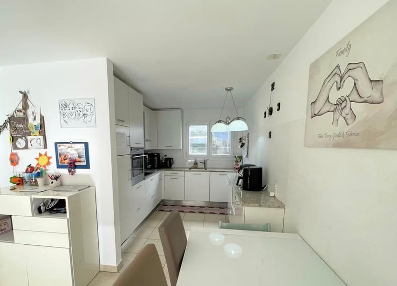 modern kitchen with white cabinets, granite countertops, stainless steel appliances, dining area with table and chairs, decorative wall art