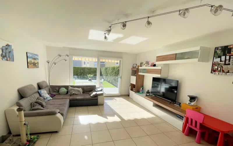 modern living room with a large sofa, a flat screen TV, a coffee table, and a view of the garden