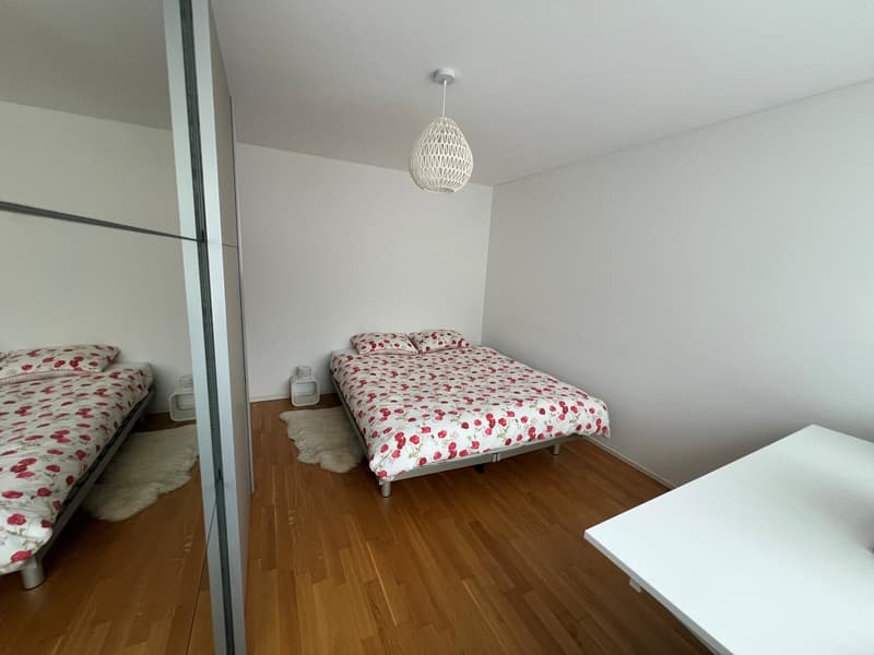 Bedroom with two single beds, white walls, wooden floor, white rug, white table, white lamp