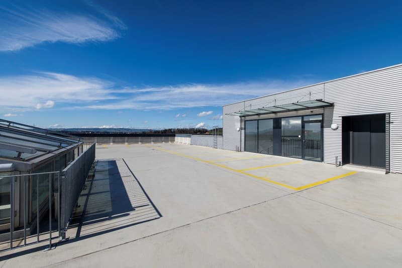 A building with a parking lot, railings on one side, glass doors and windows
