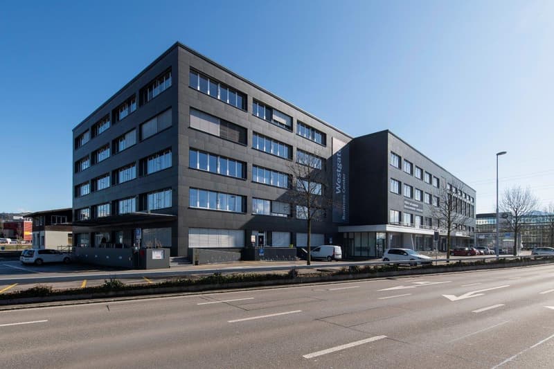 modern office building with multiple windows, concrete facade, ground floor entrance, parking area