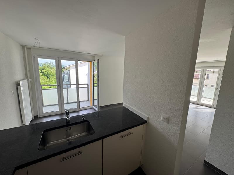 Empty kitchen with black countertop, silver sink, glass doors leading to balcony