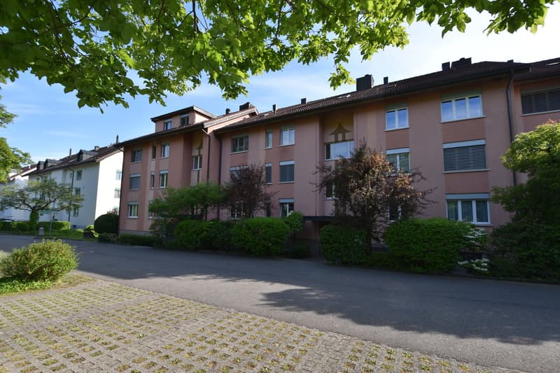 A block of apartment buildings with several floors and windows, located in a residential area, surrounded by bushes and trees.