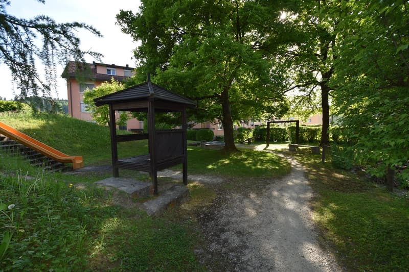 pathway, gazebo, slide, swing, benches, grassy lawn, trees, building in the background