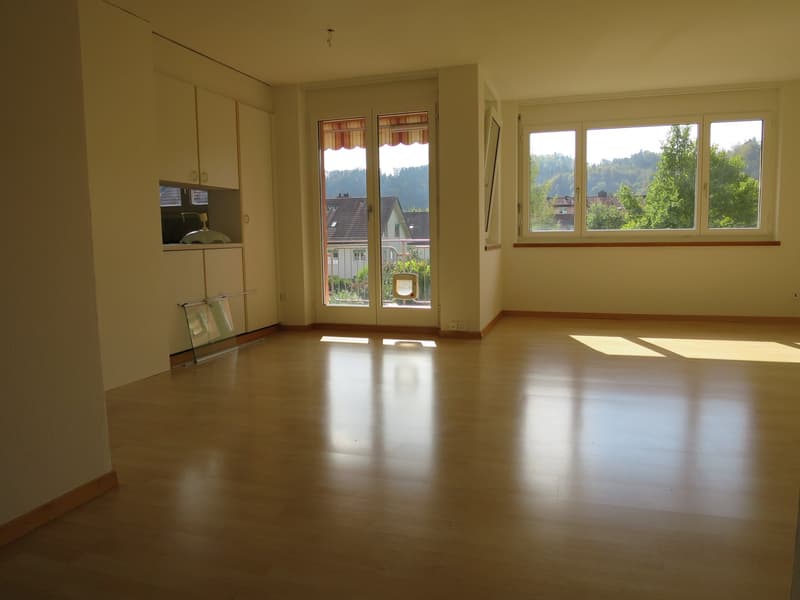 Empty room, wooden floor, sliding glass door with balcony, windows, white ceiling, cabinets, power outlet.
