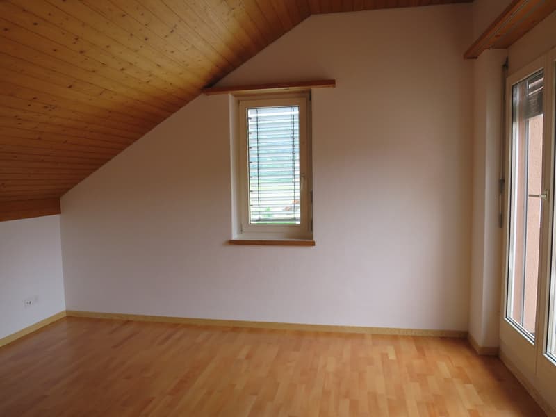 room with sloped ceiling, wooden floor, white walls, window with wooden frame, entrance door