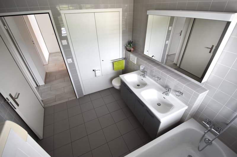 Two sinks, bathtub, large mirror, cabinet with towel
