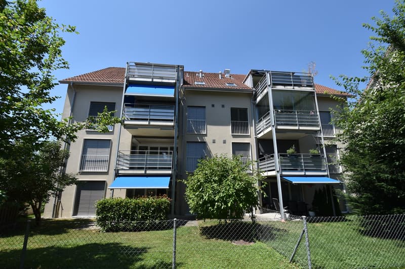 apartment building, brown roof, blue awnings on balconies, garden in front