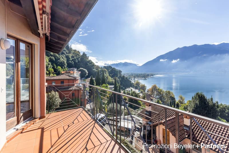 Spacious balcony with wooden flooring, overlooking a scenic lake surrounded by mountains and lush greenery. The balcony offers a panoramic view of the beautiful natural landscape.