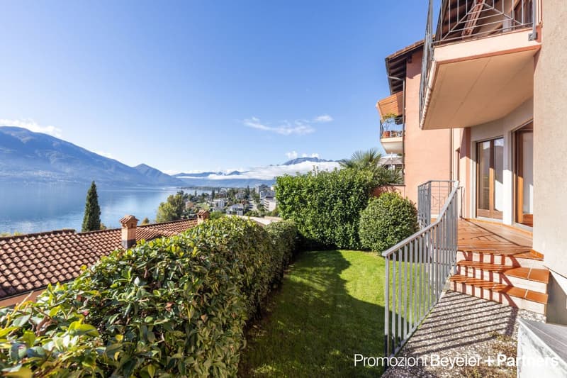 2-story residential building with a balcony, surrounded by lush greenery and offering a scenic view of the lake and mountains in the background