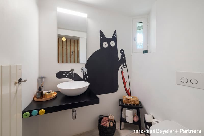 white wall, black cat art on wall, white sink, white toilet, black counter