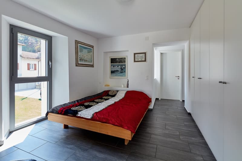 bedroom with bed, window, white walls, wooden floor, white wardrobes, paintings on the wall