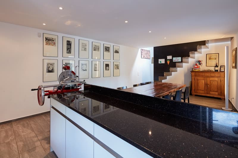 modern kitchen with black granite countertop, wooden dining table, chairs, wooden cabinet, staircase, wall art