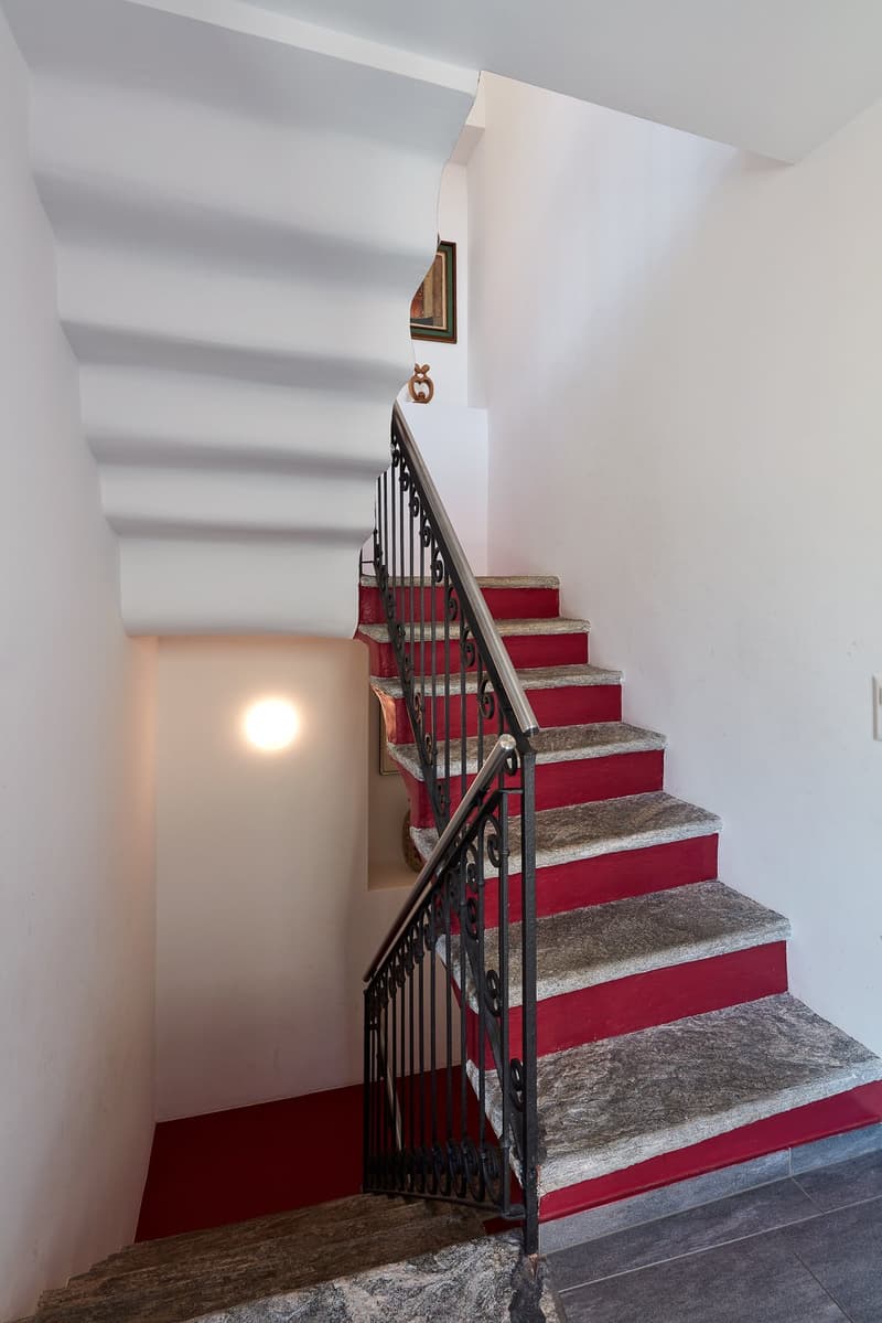 Red carpeted staircase with black railing, white walls, red steps, gray steps