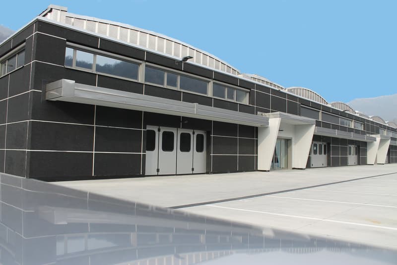 Large modern commercial building with a sleek, angular design. The building has a black and gray exterior with large windows and multiple entrances. There appears to be a garage or loading dock area on the ground floor.