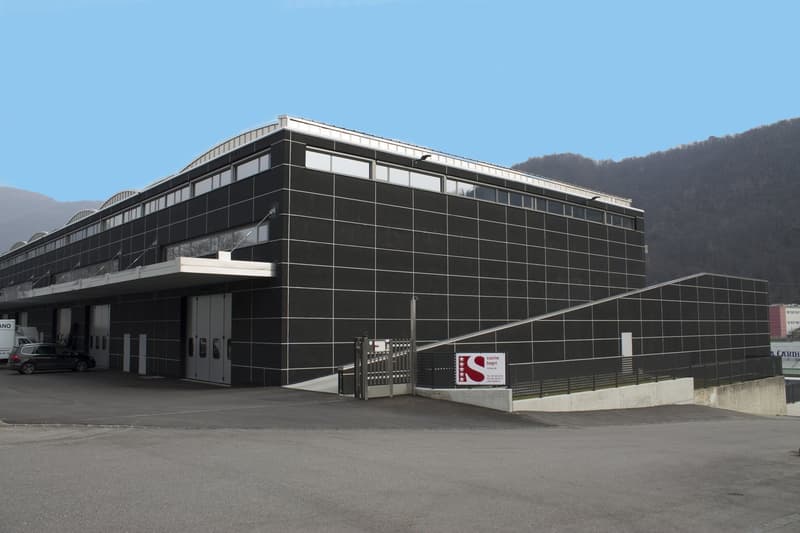 Large multi-story commercial building with a black and white facade, surrounded by a parking lot. The building appears to be a business or industrial facility.