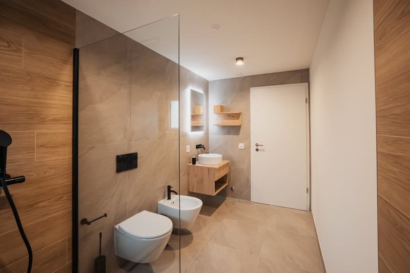 Modern bathroom with large glass shower, wooden vanity with vessel sink, shelves, and white toilet