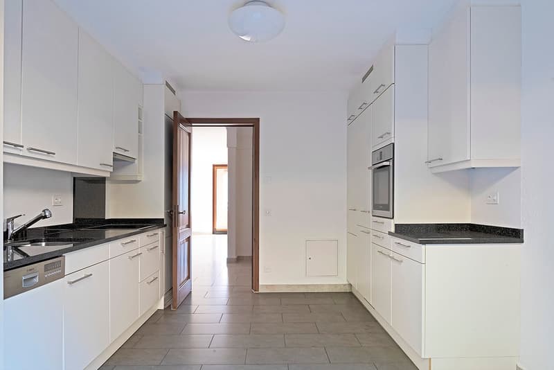 Spacious kitchen with white cabinets, black granite countertops, built-in dishwasher, and tile flooring. The kitchen opens up to another room through a doorway.