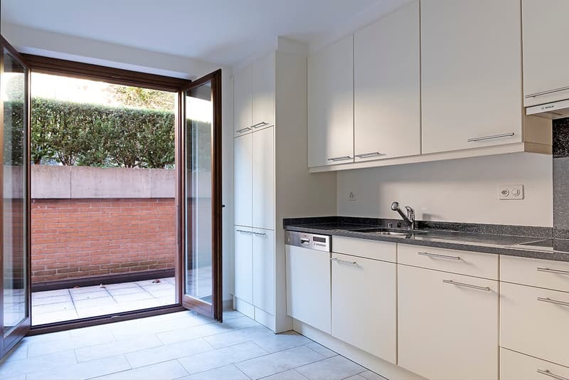 Modern kitchen with white cabinets, granite countertop, stainless steel appliances, and sliding glass door leading to a balcony or terrace area.