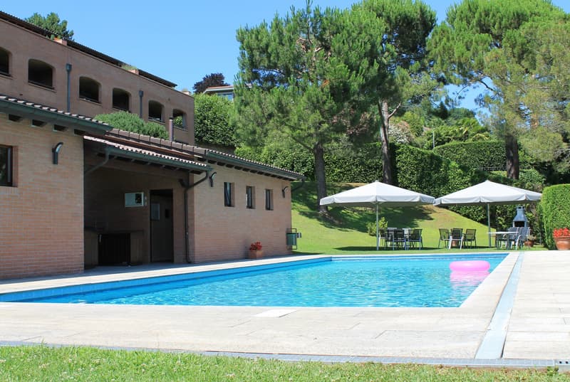 Brick building, swimming pool, outdoor dining area, umbrellas, trees, green lawn