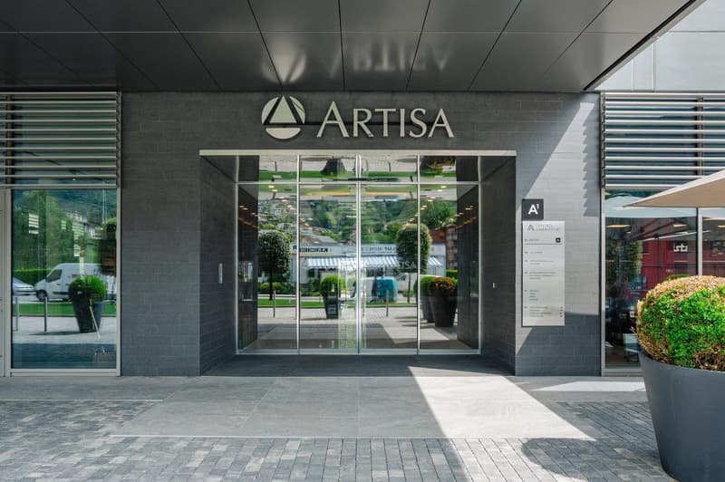 modern building entrance, large glass doors, gray stone walls, Artisa sign, potted plants, reflective windows