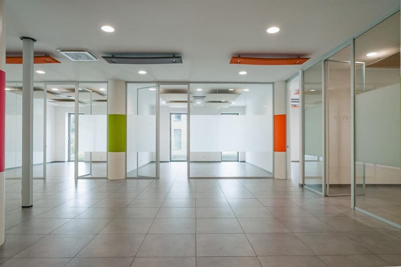Large empty office space, tile flooring, white walls, glass walls, central pillars