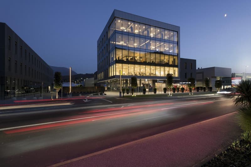 modern office building with glass facades, well-lit windows, several floors, landscaped entrance, modern architecture