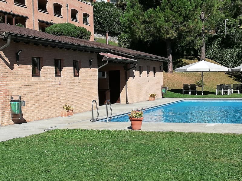 brick house, swimming pool, large umbrellas, chairs, green lawn, potted plants