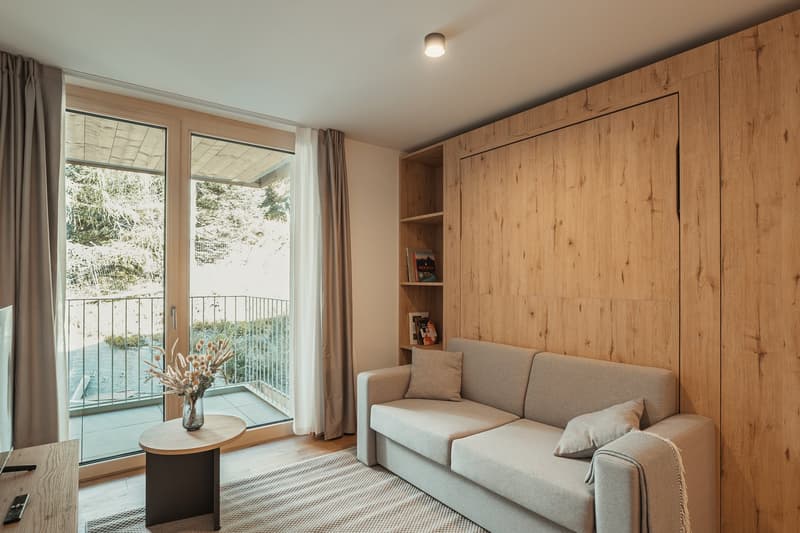 Modern living room with wooden walls, a couch, side table, and a balcony with a railing.