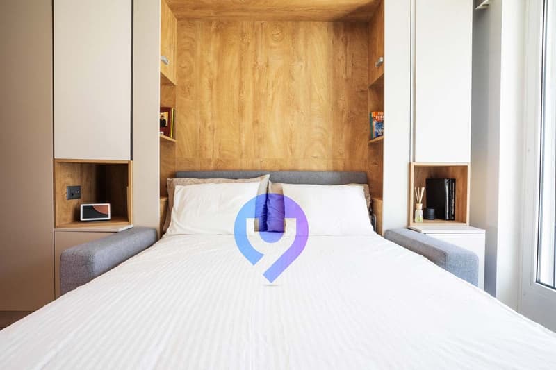 Wooden paneled walls, white bedding, gray side tables, built-in shelving units