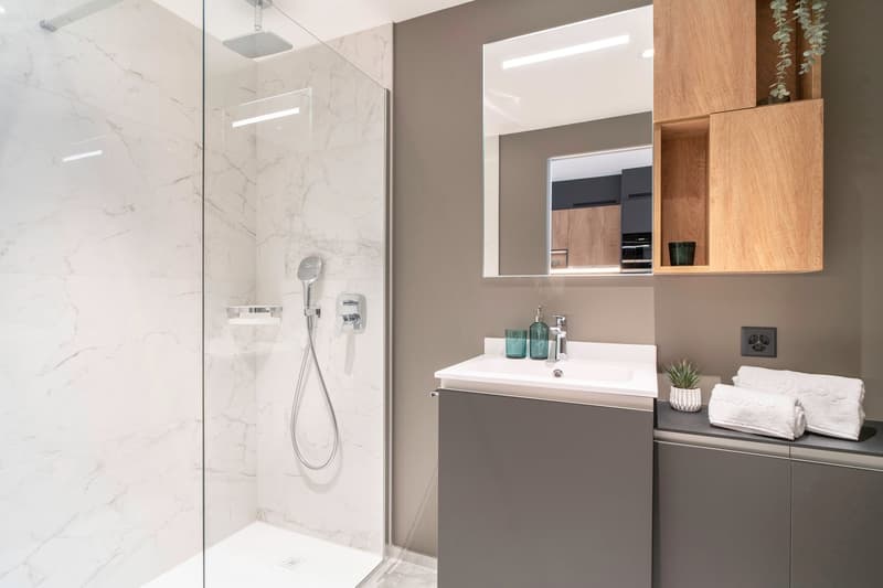 Modern bathroom with marble-like tiles, glass shower enclosure, vanity unit with sink, and built-in storage cabinets