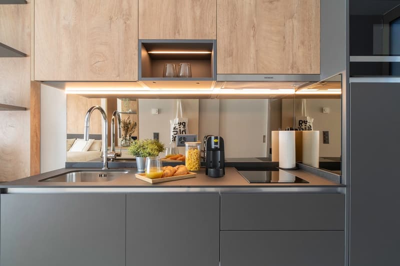 Modern kitchen with wooden cabinets, stainless steel appliances including a dishwasher, and a countertop with various kitchen items such as a coffee maker, flowers, and baked goods.