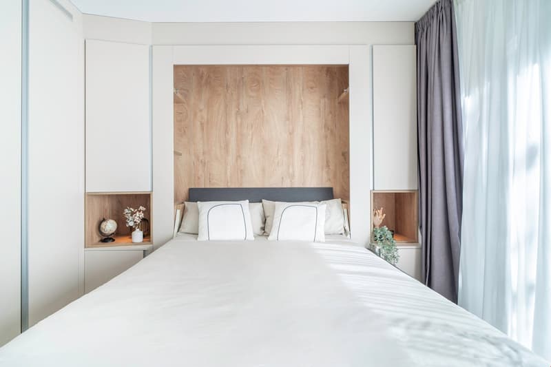 Spacious bedroom with a wooden accent wall, white bedding, side tables, and curtains. The room has large windows that provide natural light and access to a balcony or terrace.