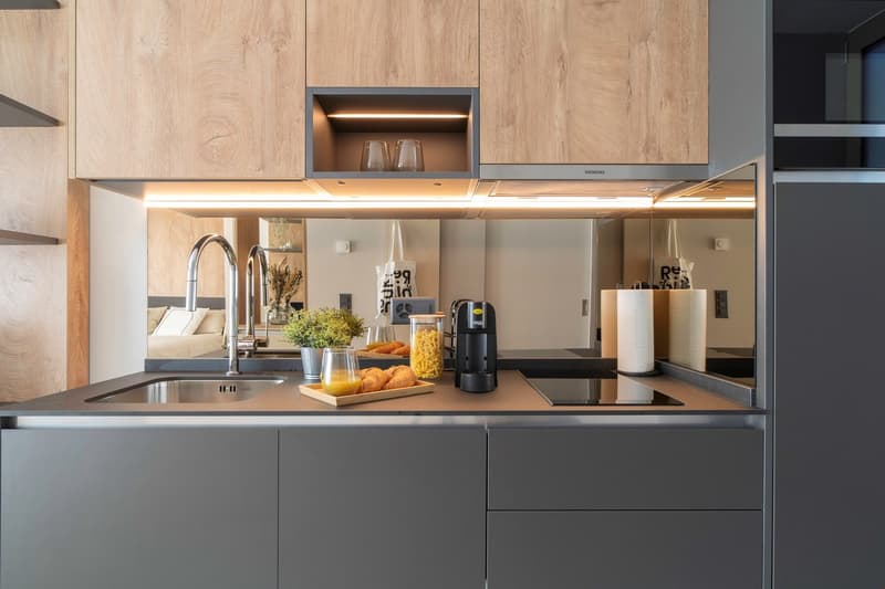 Modern kitchen with wooden cabinets, stainless steel appliances including a dishwasher, a sink with chrome faucet, and various kitchen accessories and decor items on the countertop.