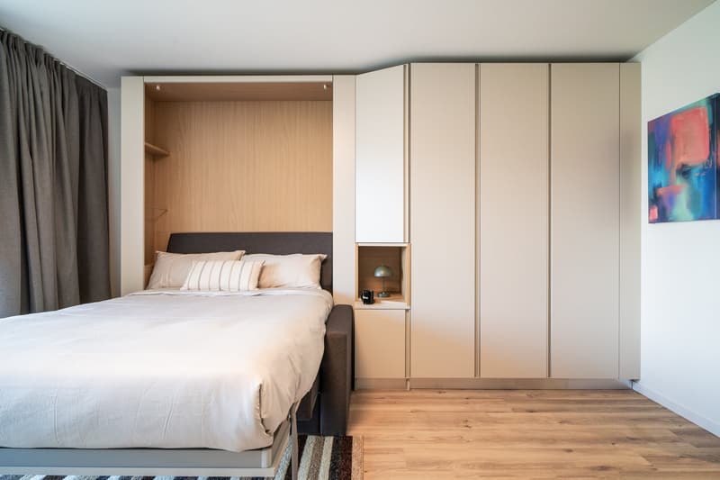 Spacious bedroom with a large bed, built-in wardrobe, and hardwood flooring. The room features a balcony or terrace, providing natural light and access to the outdoors.